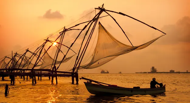 Chinese fishing nets at sunset in Kochi, India, silhouetted against the glowing sky and calm water