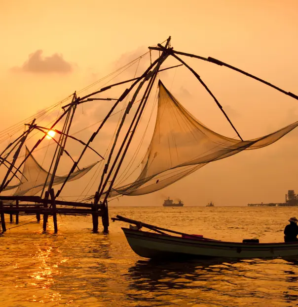 Chinese fishing nets at sunset in Kochi, India, silhouetted against the glowing sky and calm water