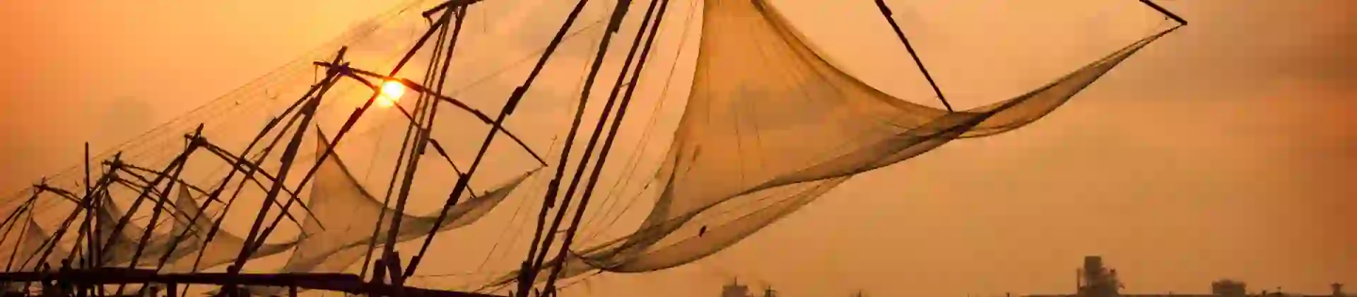 Chinese fishing nets at sunset in Kochi, India, silhouetted against the glowing sky and calm water