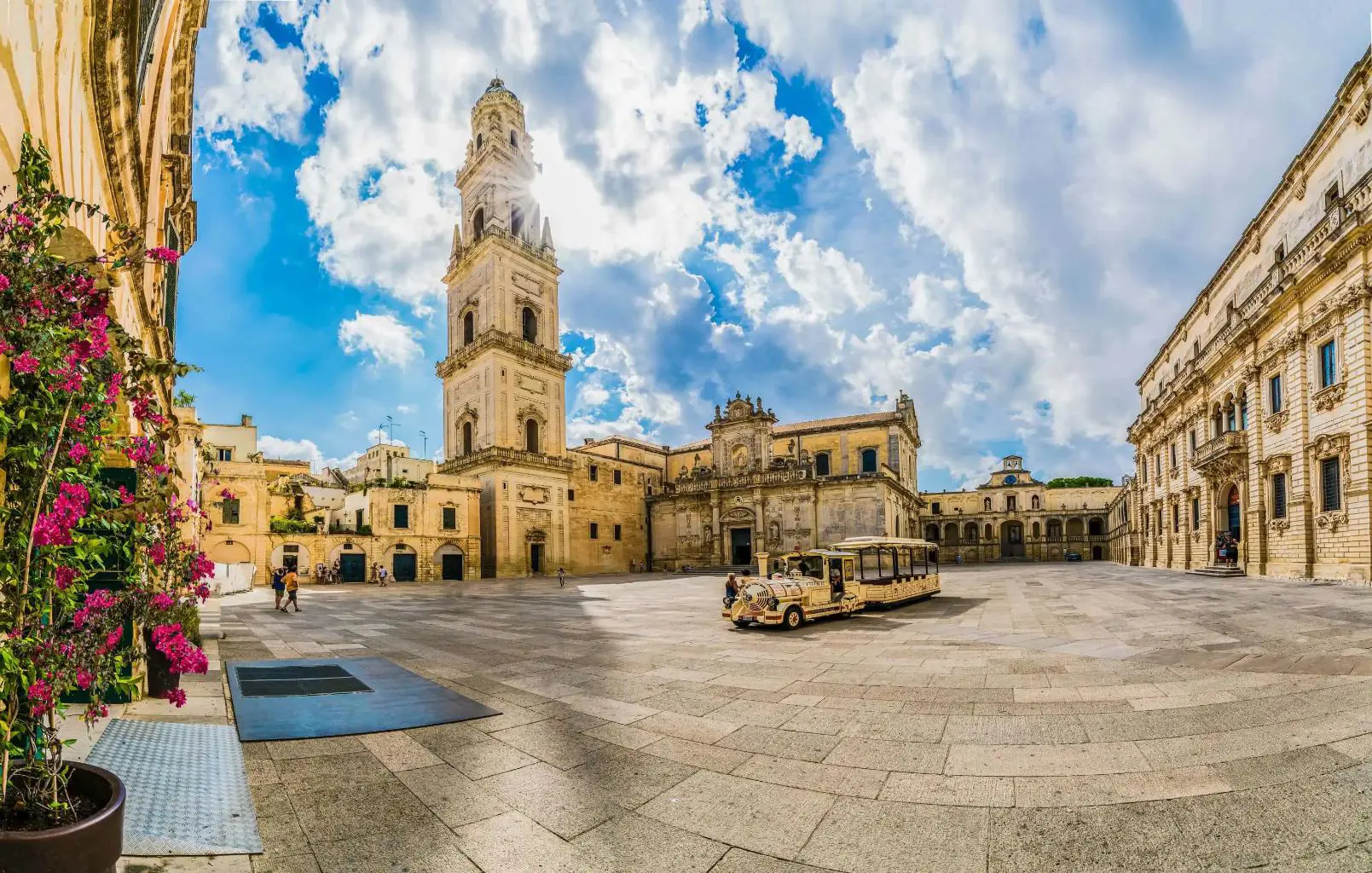 A square in Lecce, Puglia, Italy, featuring a historic tower and a land train for tourists