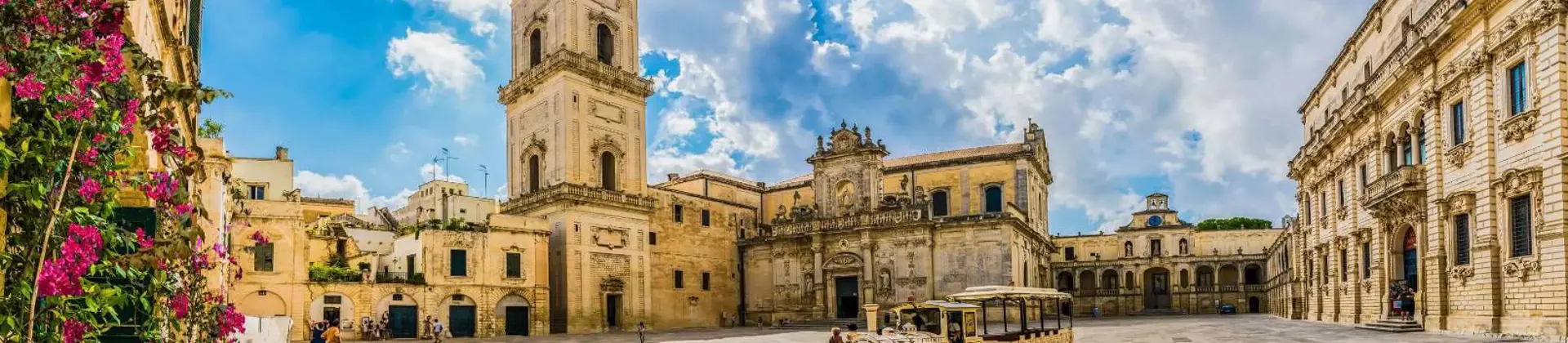 A square in Lecce, Puglia, Italy, featuring a historic tower and a land train for tourists