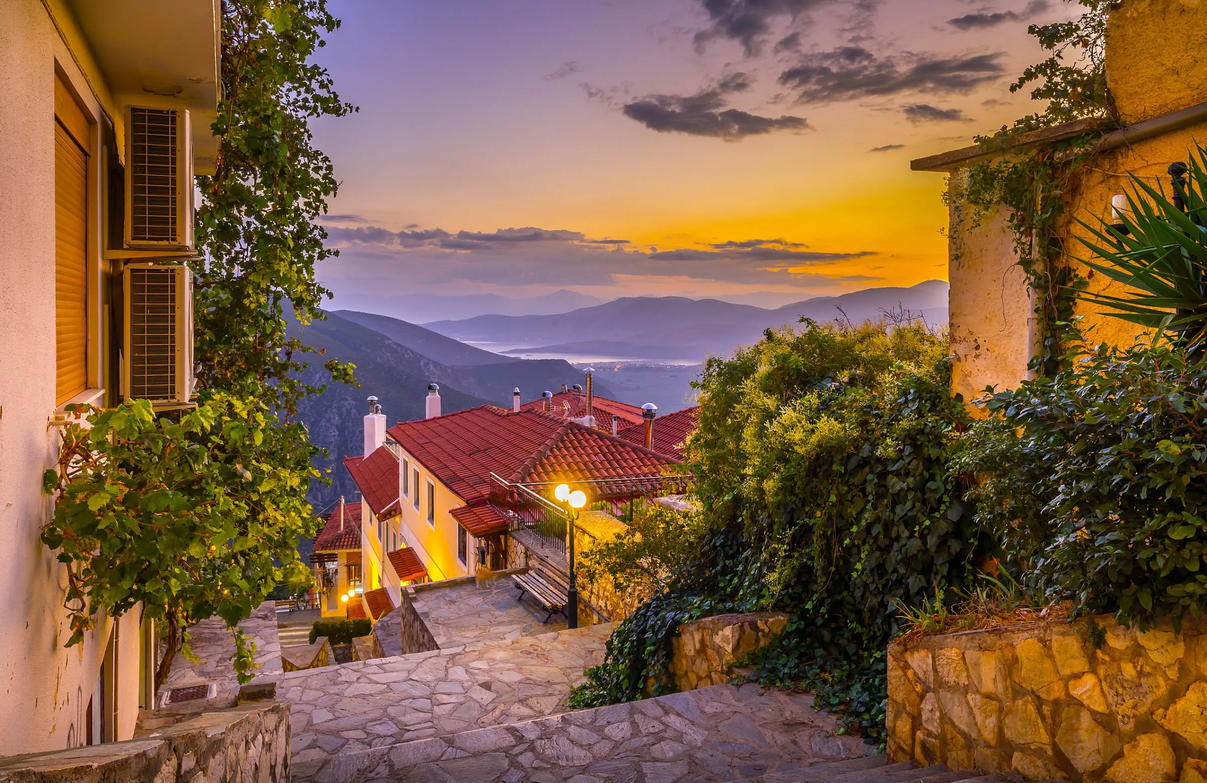 View from Delphi in the mountains, looking out on the landscape with sunset and silhouette of mountains. Steps and buildings in the forefront