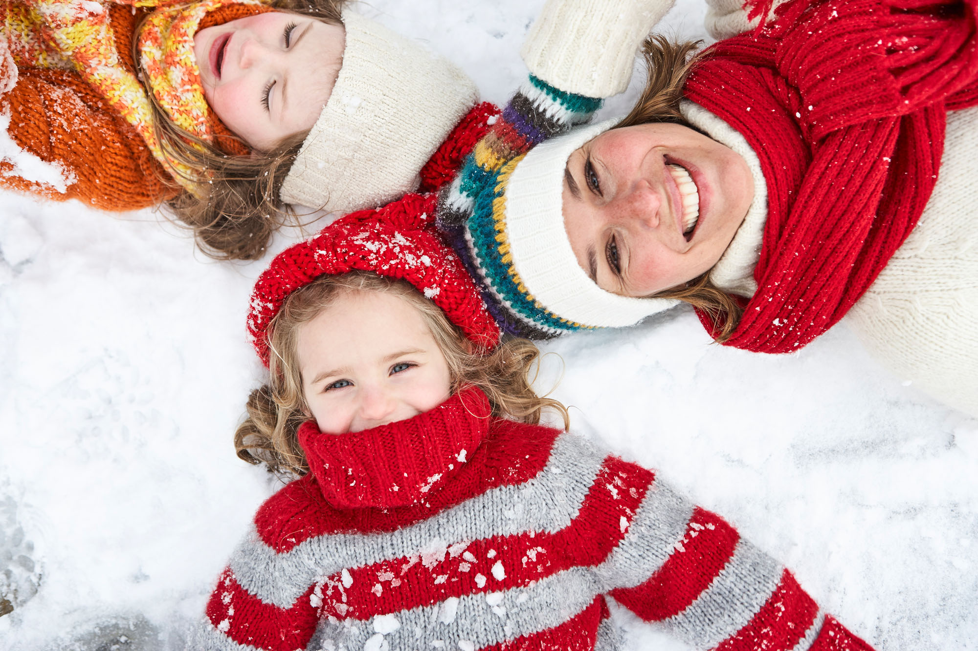 Face-shot of mother and two children lying in the snow, looking into the camera, laughing