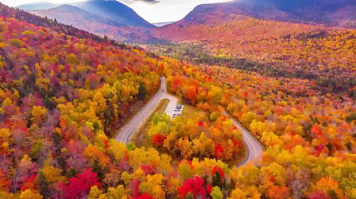 Kancamagus Highway in New Hampshire lined with vibrant autumn foliage, featuring a winding road surrounded by trees in shades of red, orange, and yellow