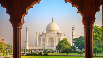 The Taj Mahal framed by an ornate archway, with green gardens in the foreground
