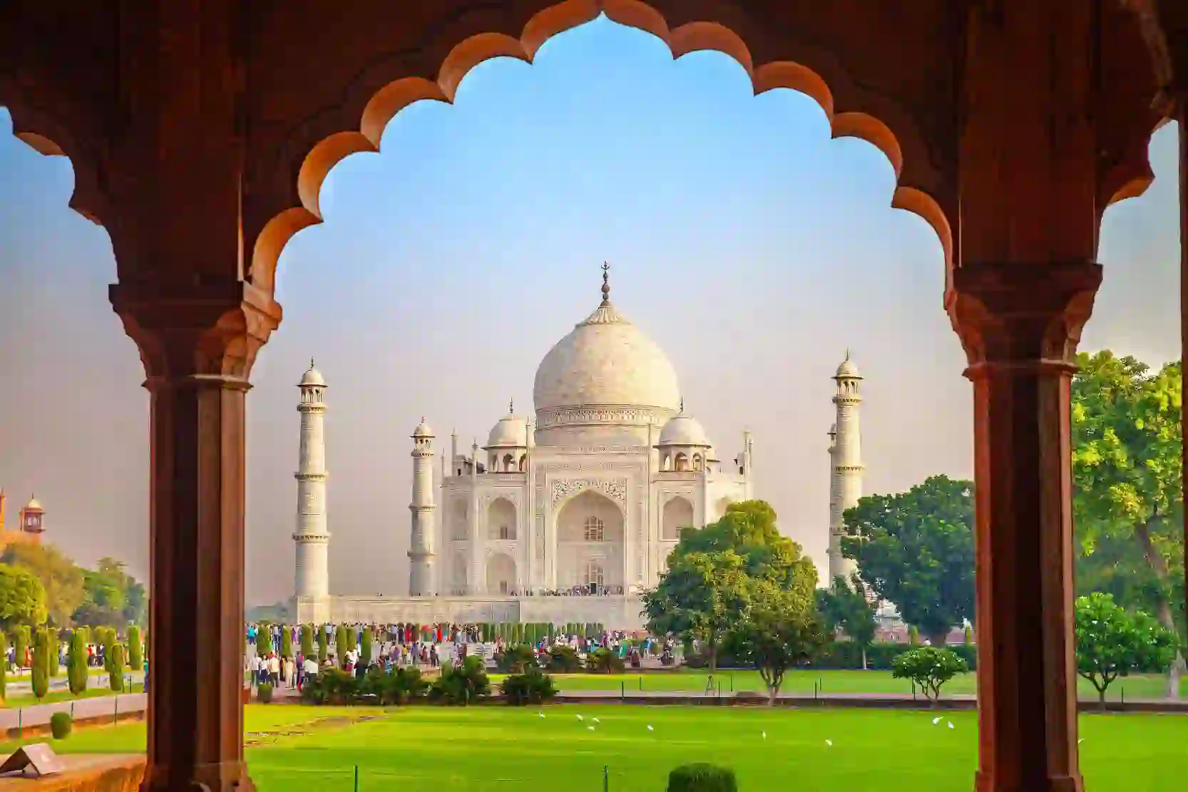 The Taj Mahal framed by an ornate archway, with green gardens in the foreground