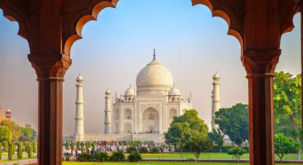 The Taj Mahal framed by an ornate archway, with green gardens in the foreground