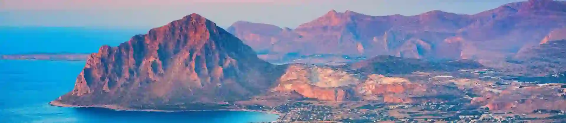 Mountain landscape of Erice, Sicily, showing a rugged hill with green vegetation and buildings clustered near the coastline below
