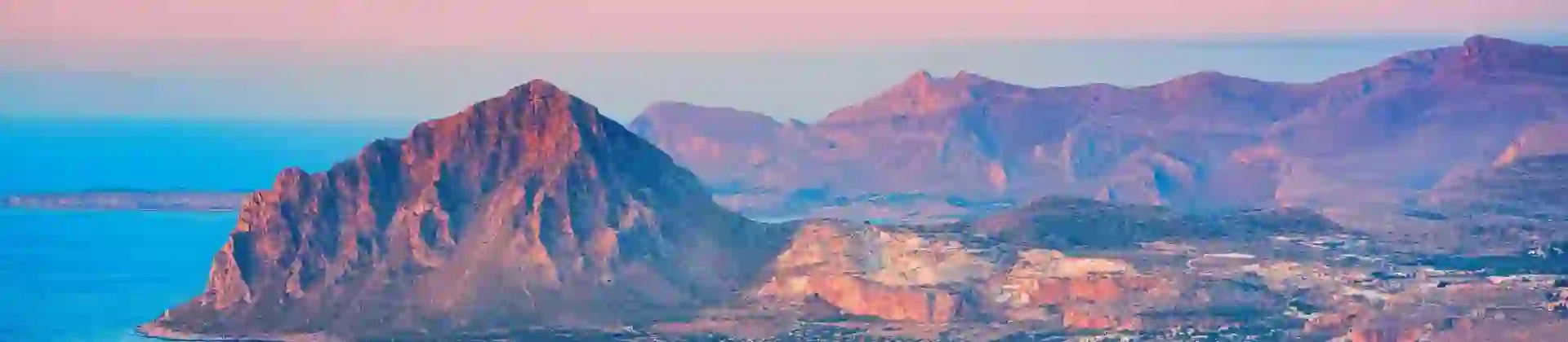 Mountain landscape of Erice, Sicily, showing a rugged hill with green vegetation and buildings clustered near the coastline below