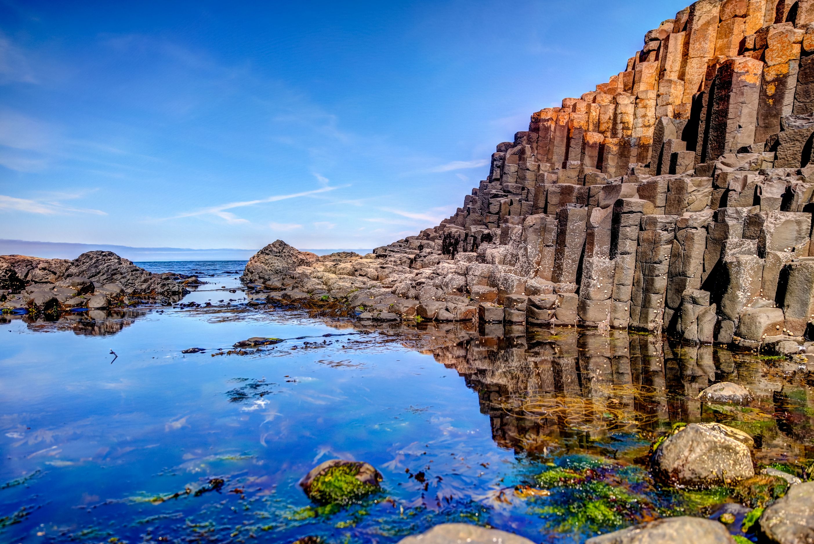 Hexagonal basalt columns of the Giant’s Causeway in Northern Ireland by a calm tidal pool reflecting the clear sky and rock formations