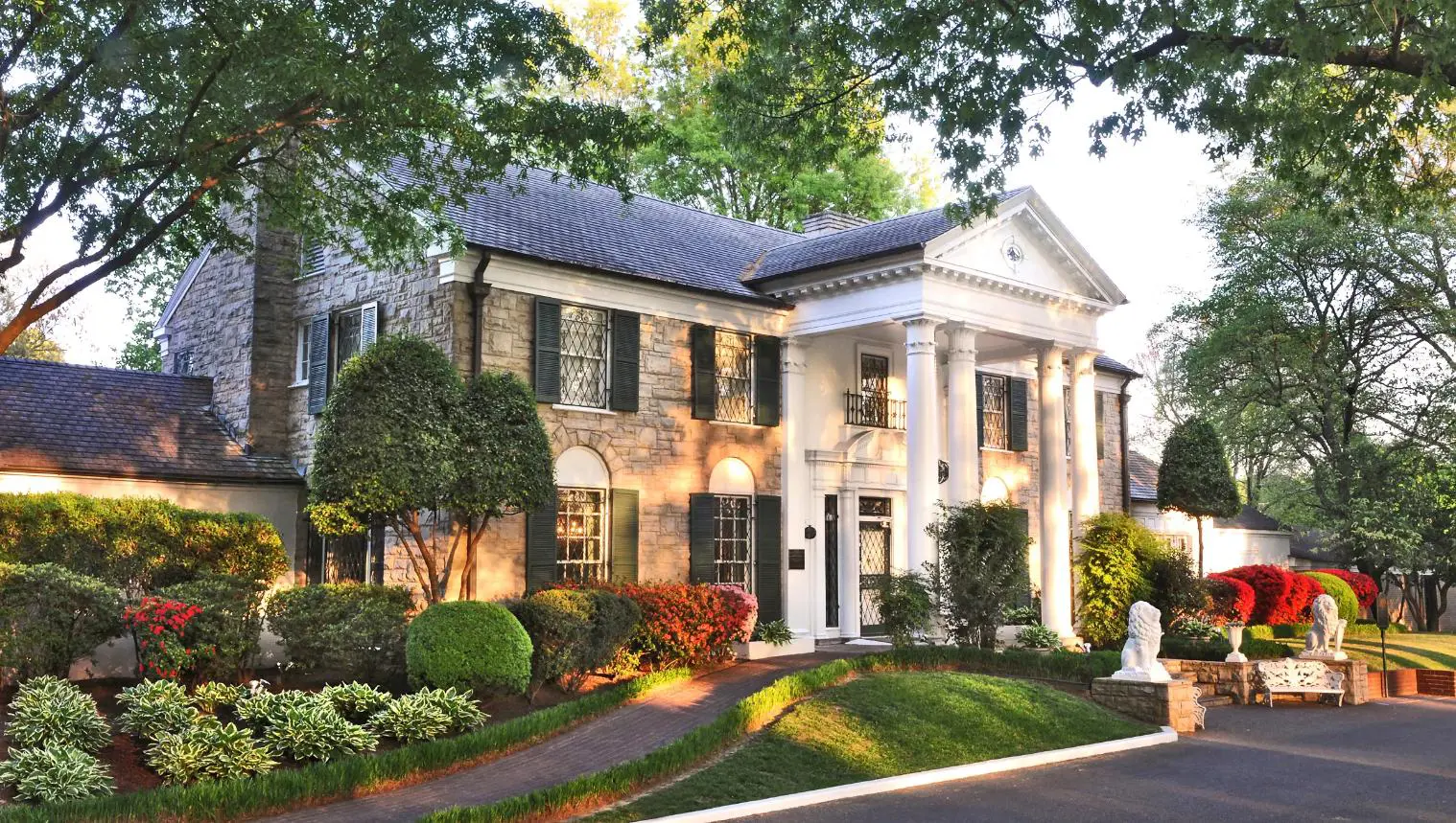 Front view of Graceland, Elvis Presley’s historic mansion in Memphis, Tennessee, surrounded by lush landscaping and white columns.