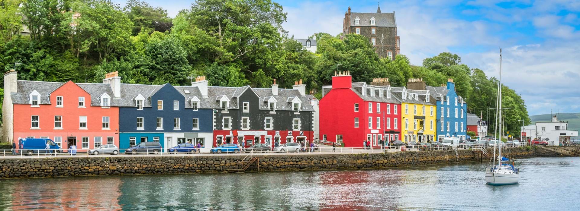 Colourful buildings along the waterfront in Tobermory, Isle of Mull, with a sailboat on the water 