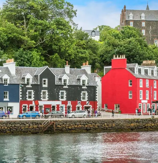 Colourful buildings along the waterfront in Tobermory, Isle of Mull, with a sailboat on the water 