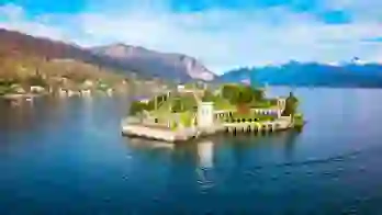 A picturesque view of Isola Bella on Lake Maggiore in Italy, featuring its ornate terraced gardens, elegant architecture and the surrounding mountains reflected in the water