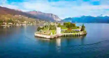 A picturesque view of Isola Bella on Lake Maggiore in Italy, featuring its ornate terraced gardens, elegant architecture and the surrounding mountains reflected in the water