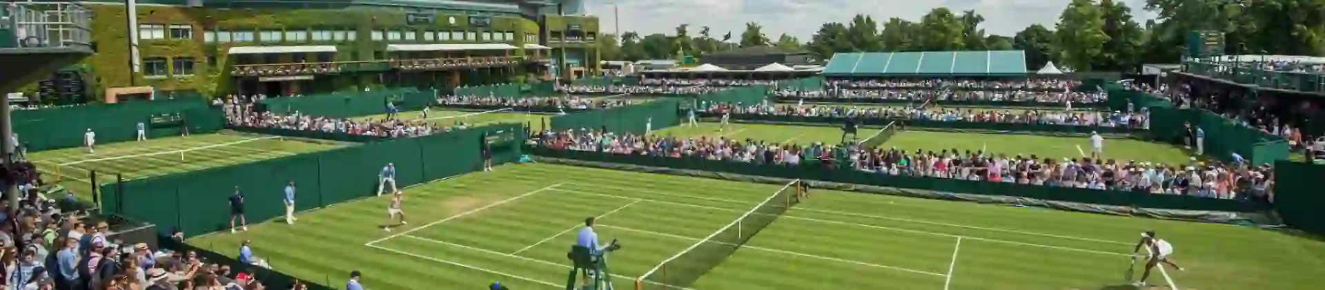 Crowds watching tennis matches on the grass courts at Wimbledon under a blue sky