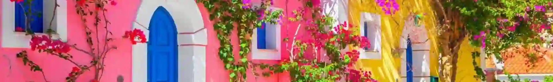 Pink house and a yellow house, with blue front doors and Juliette balconies. Pink and purple flowers growing against them.