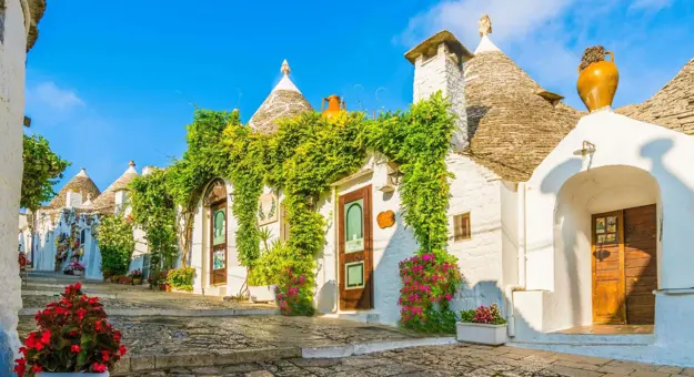 View of traditional white Trulli houses with conical stone roofs in Alberobello, Apulia, Italy, under a clear blue sky