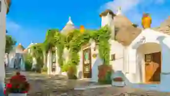 View of traditional white Trulli houses with conical stone roofs in Alberobello, Apulia, Italy, under a clear blue sky