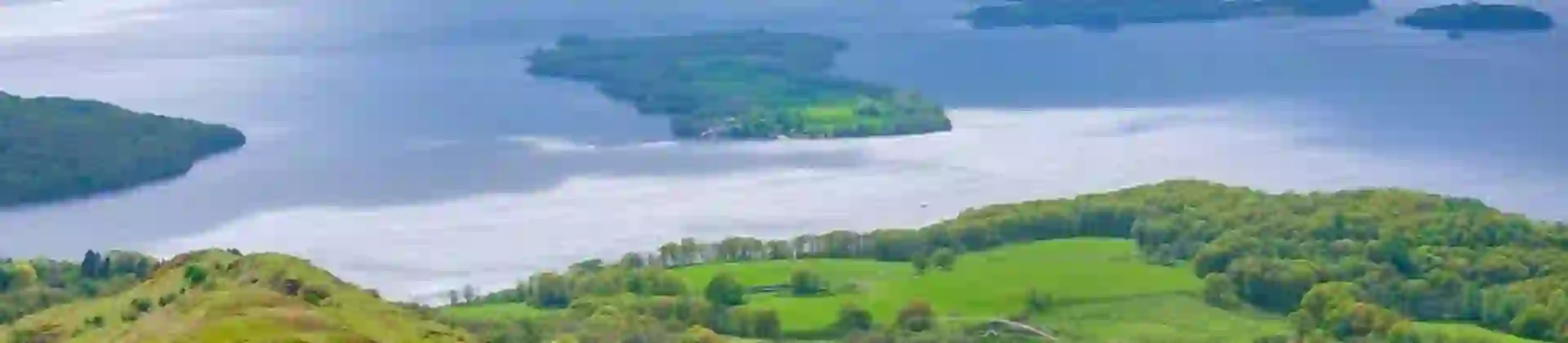 High angle view of Loch Lomond and Trossachs National Park, with a man wearing a red jacket walking down the mountain