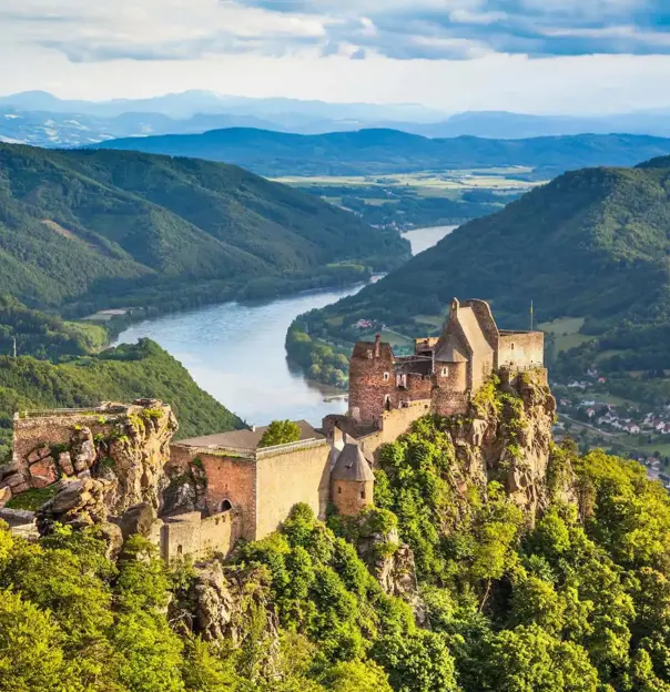 Ruins of a medieval castle perched on a rocky hilltop overlooking the Danube River in the Wachau Valley, Austria, surrounded by lush green hills and distant mountains