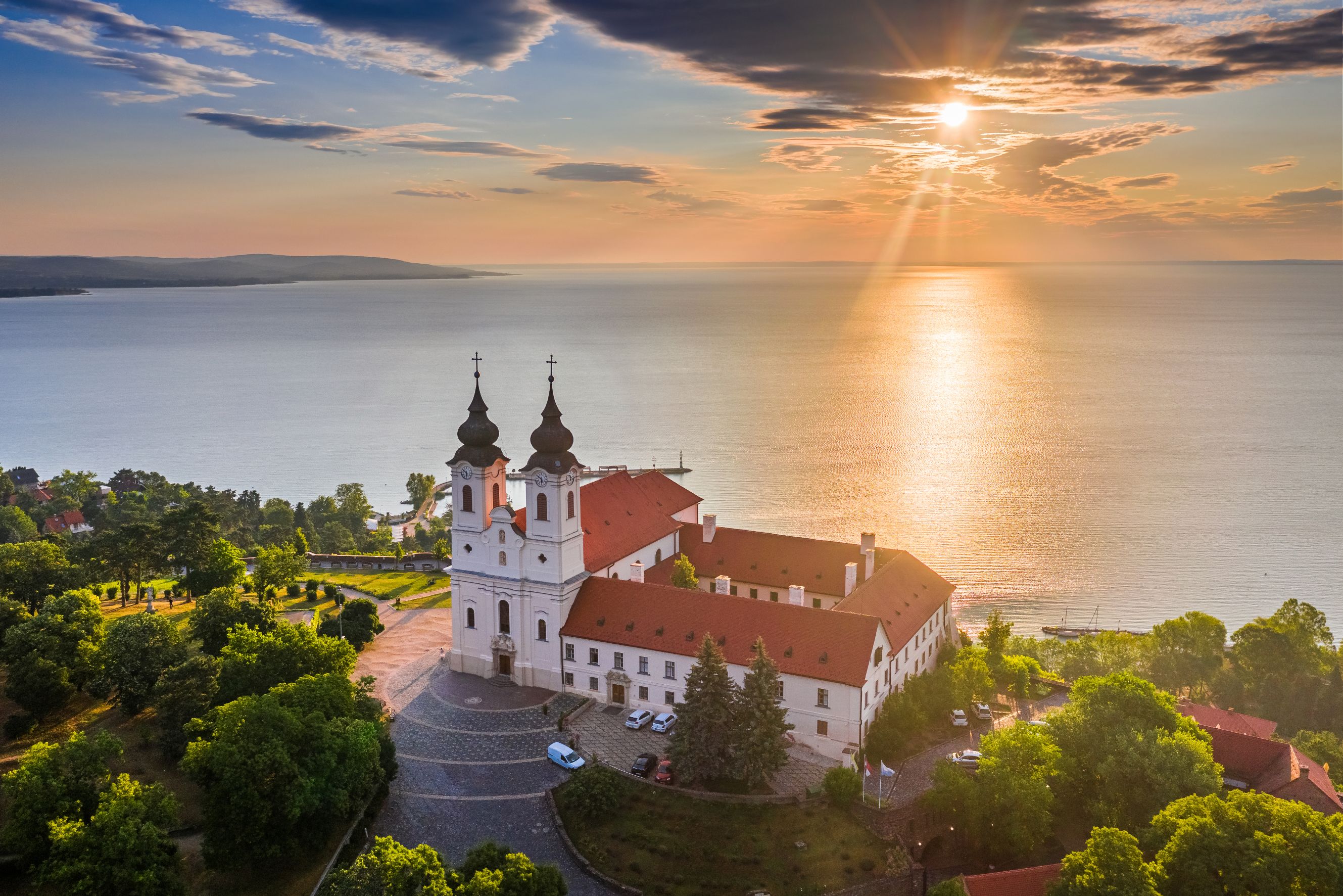 High angle shot of Lake Balaton, with a church with red roofs and two black towers on the waterfront. 