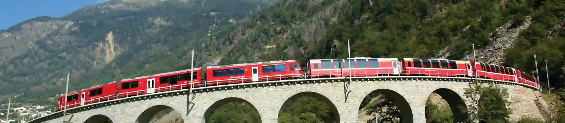 The Bernina Express going across a bridge, with grassy mountains in the background