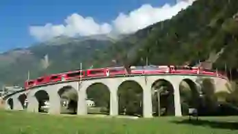 The Bernina Express going across a bridge, with grassy mountains in the background