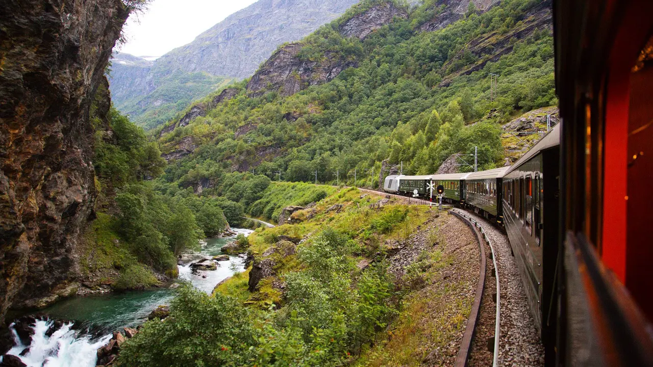 Train going through the mountains by a small stream of water