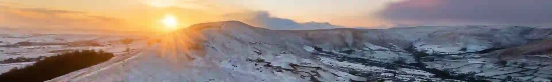 View of the Peak District at winter, with snowy mountains and the sun creeping over the edge of the land