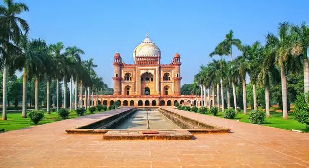 Front view of Humayun's Tomb in Delhi, India, framed by symmetrical rows of palm trees and a long reflecting pool under a clear blue sky