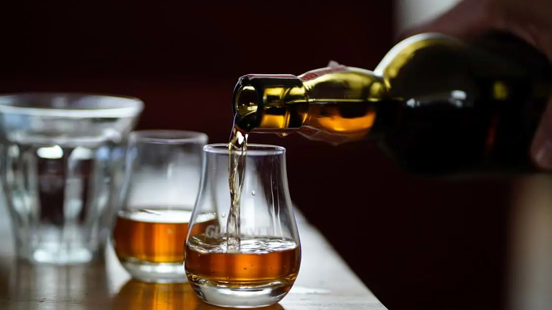 Close up of a glass of Scottish whisky being poured with dark lighting
