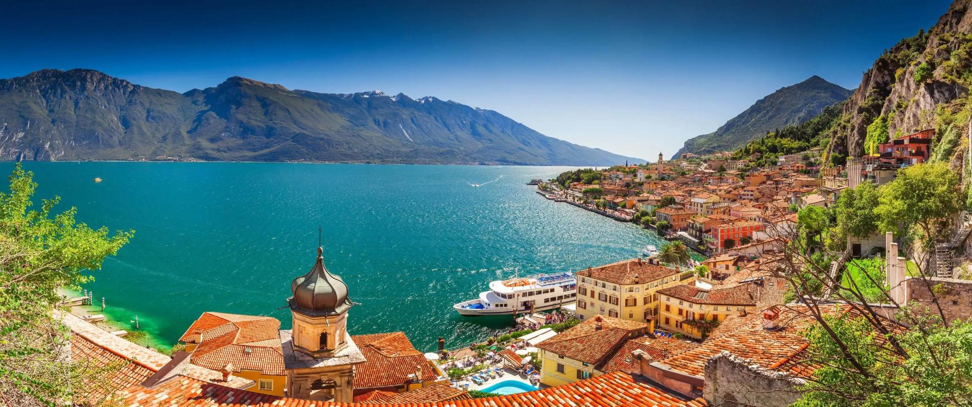 Scenic view of Limone sul Garda, a picturesque lakeside town on Lake Garda, Italy, with colourful buildings nestled against steep mountain cliffs and the calm blue lake in the foreground