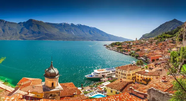 Scenic view of Limone sul Garda, a picturesque lakeside town on Lake Garda, Italy, with colourful buildings nestled against steep mountain cliffs and the calm blue lake in the foreground