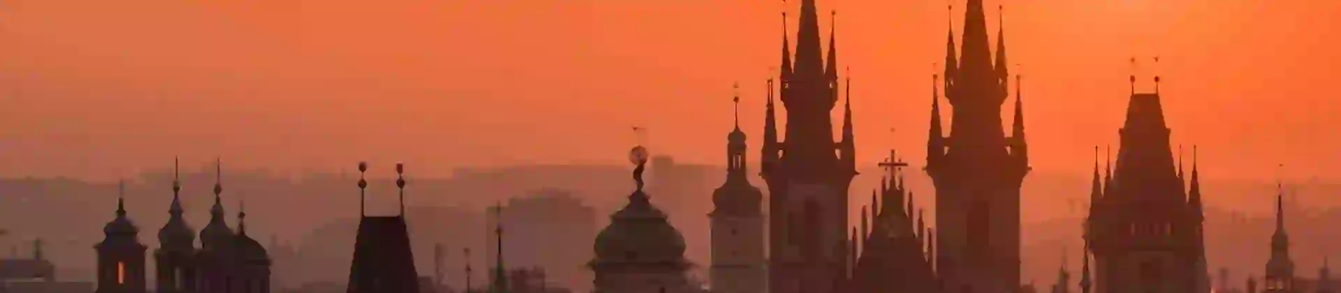 Prague cityscape against an orange sky with silhouettes of tall buildings with spiked turrets