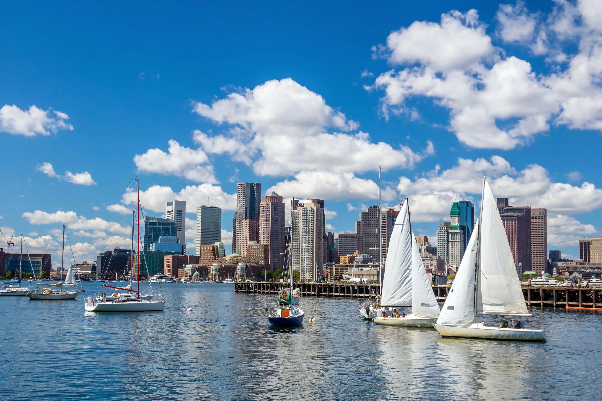 View of Boston, Massachusetts, seen across the water from Pier Park, with the city skyline rising above the harbour under a partly cloudy sky