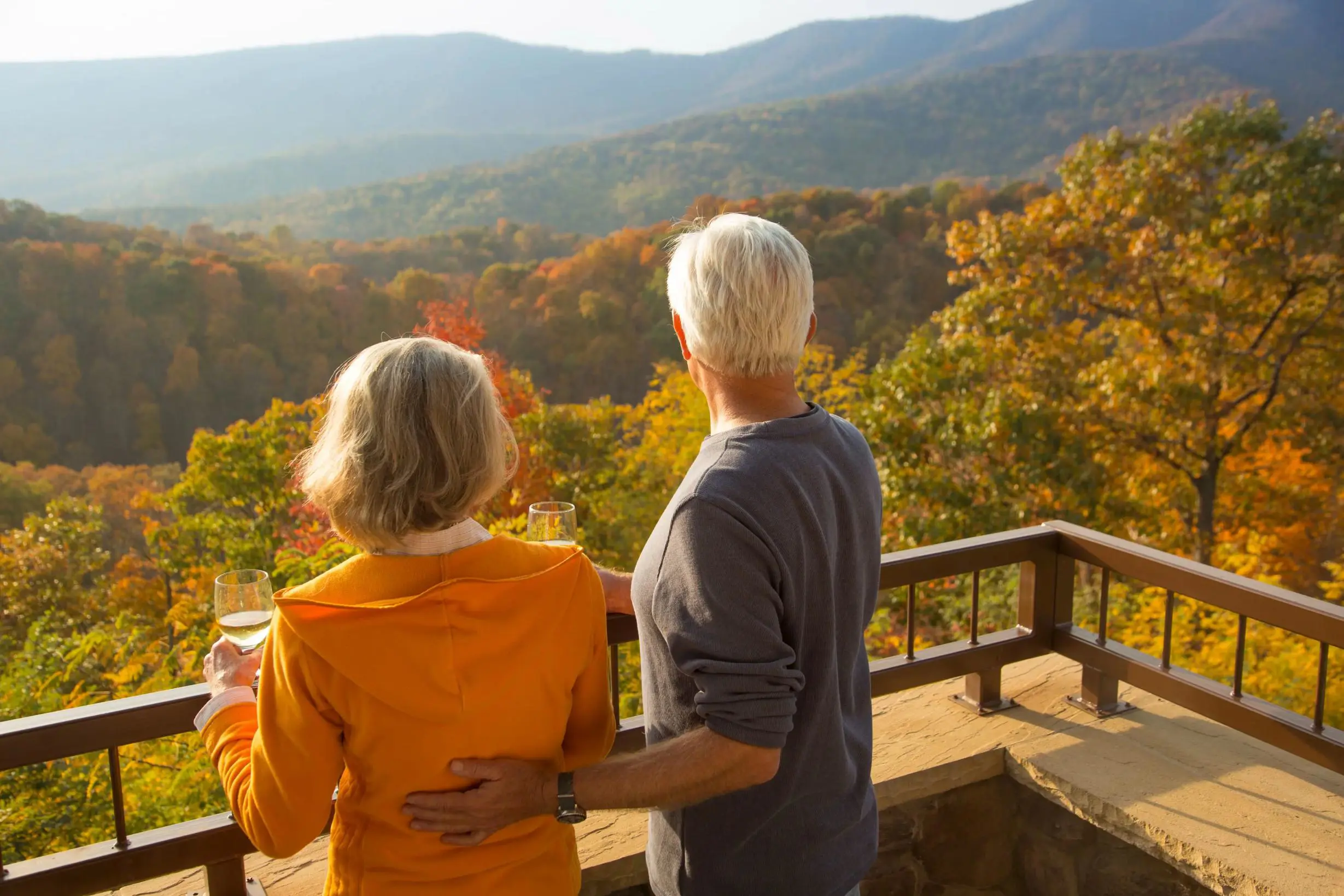 A couple enjoying a glass of wine on a terrace overlooking rolling countryside and colourful trees in New England during autumn