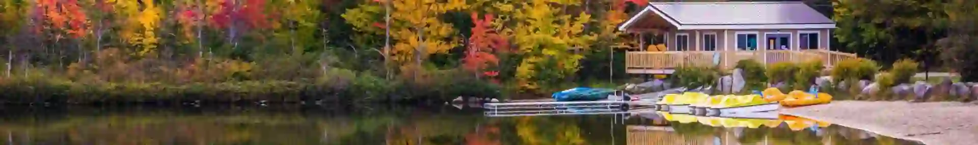 A peaceful lake reflects vibrant autumn trees and a cosy wooden cabin with kayaks on the shore in New Hampshire, USA
