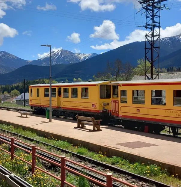 Le Train Jaune at a station with a Pyrenees mountain view