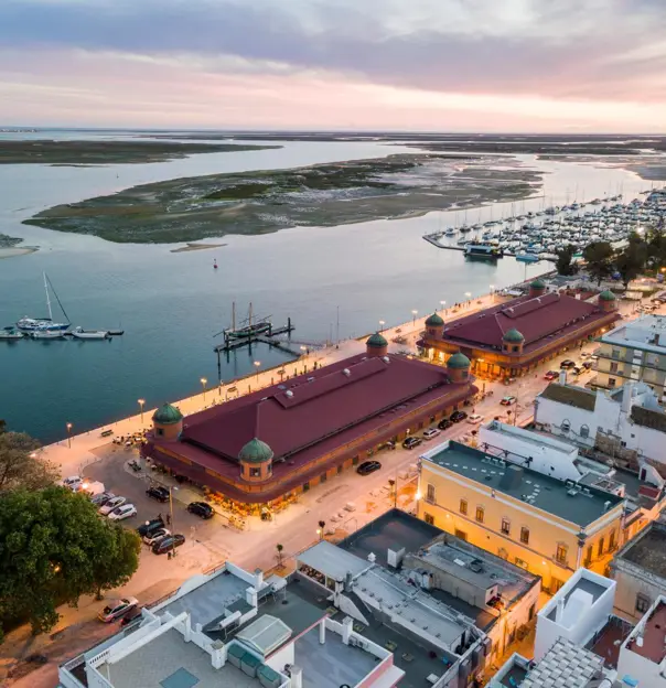 Coastline at sunset in Olhão on the Algarve, featuring a marina, small islands in view, and traditional buildings lit along the waterfront