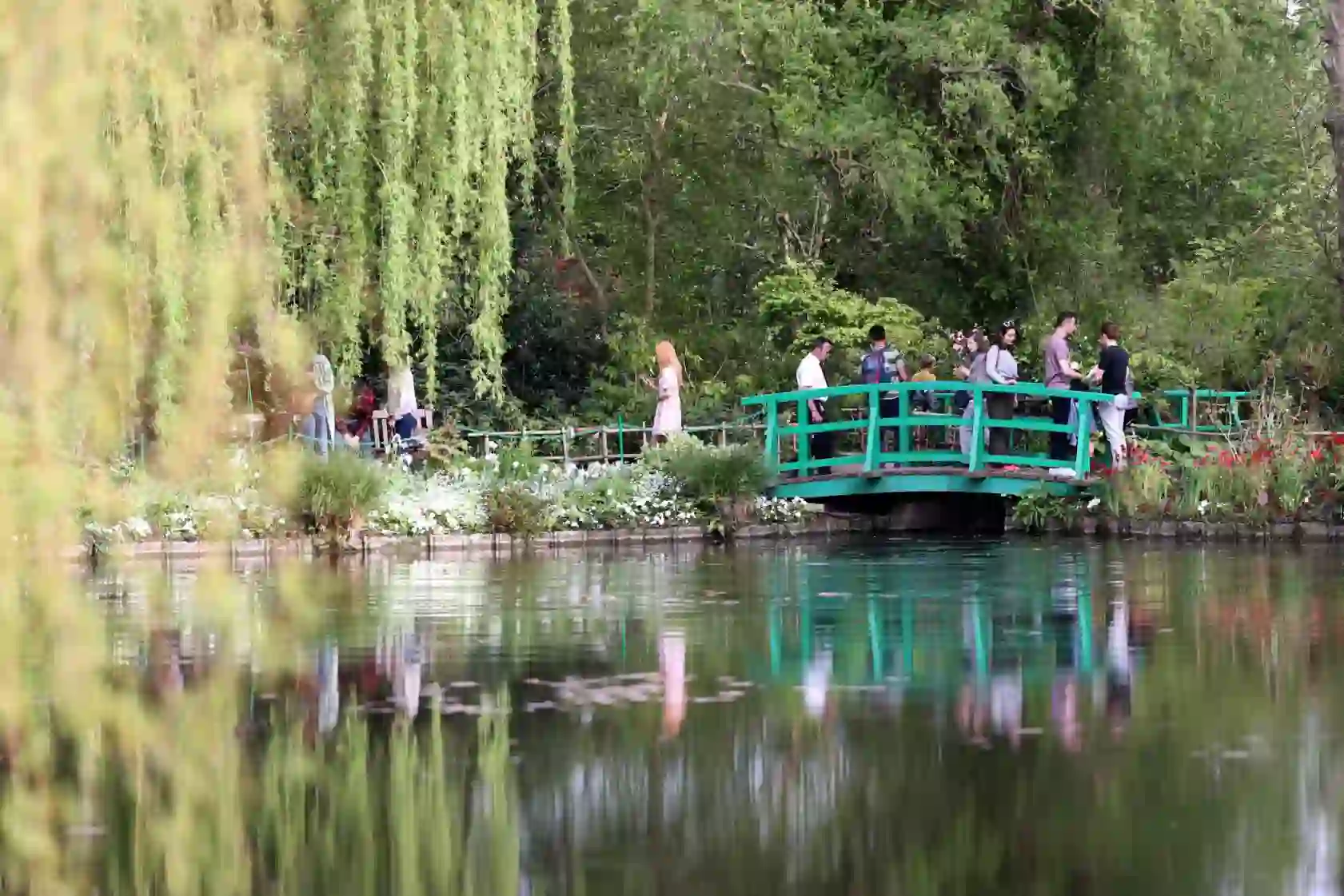 People walking over the iconic wooden bridge above the pond in Claude Monet’s gardens at Giverny