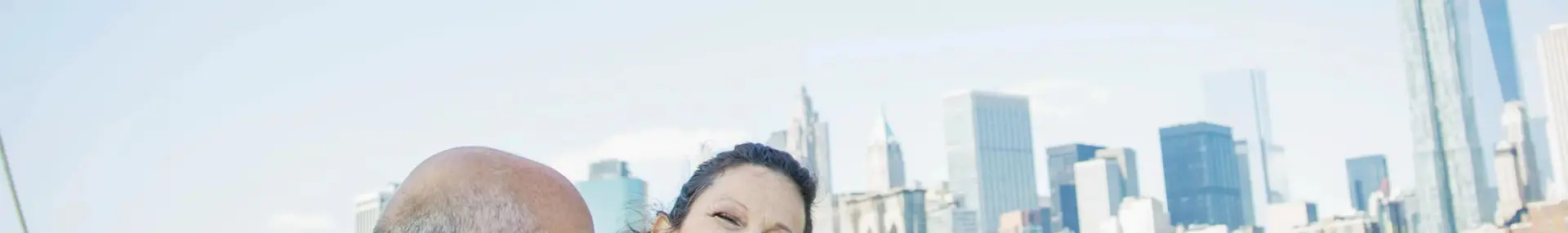 Two people smiling happily on a boat in New York City, with the city skyline visible in the background