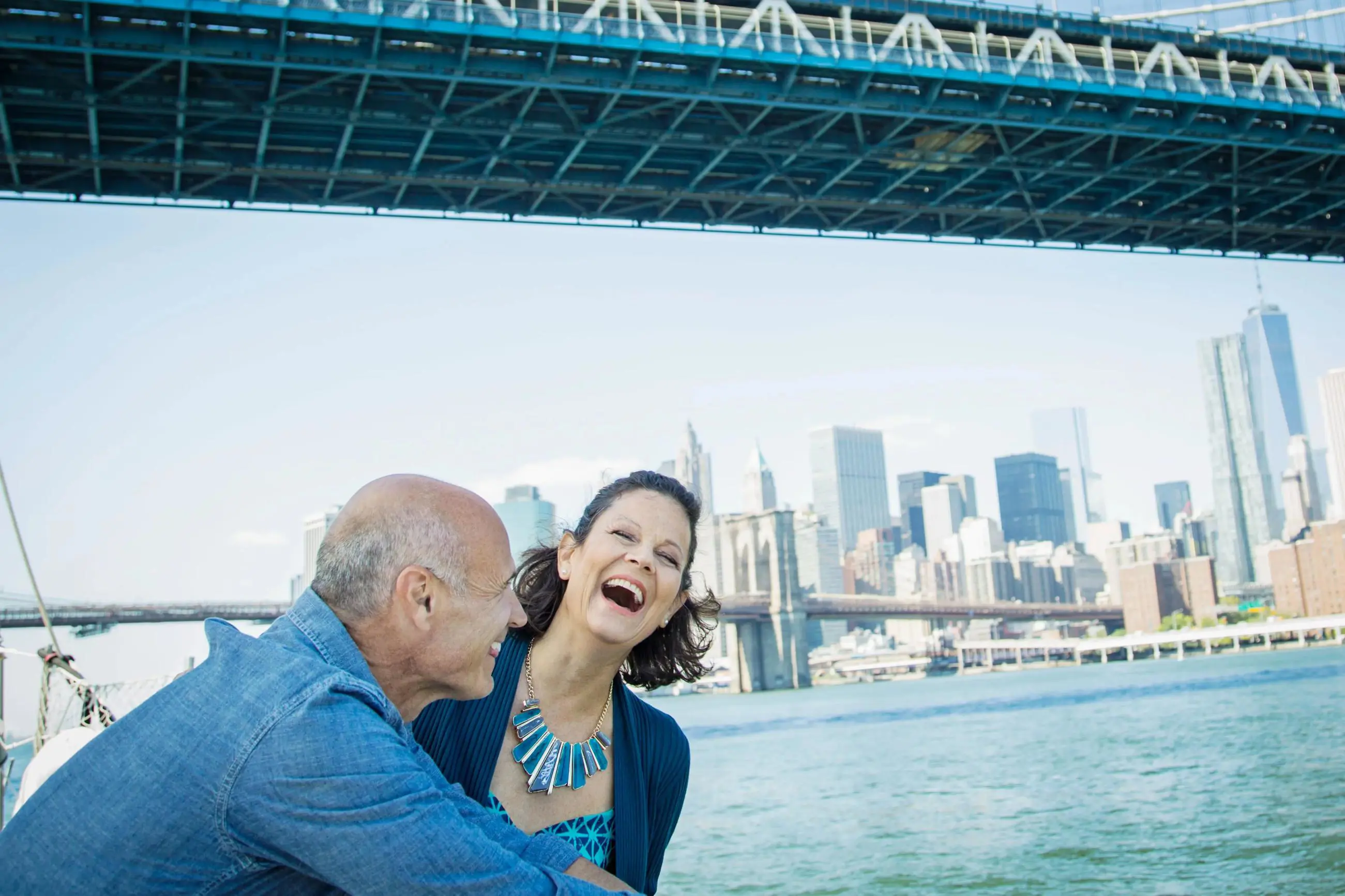 Two people smiling happily on a boat in New York City, with the city skyline visible in the background