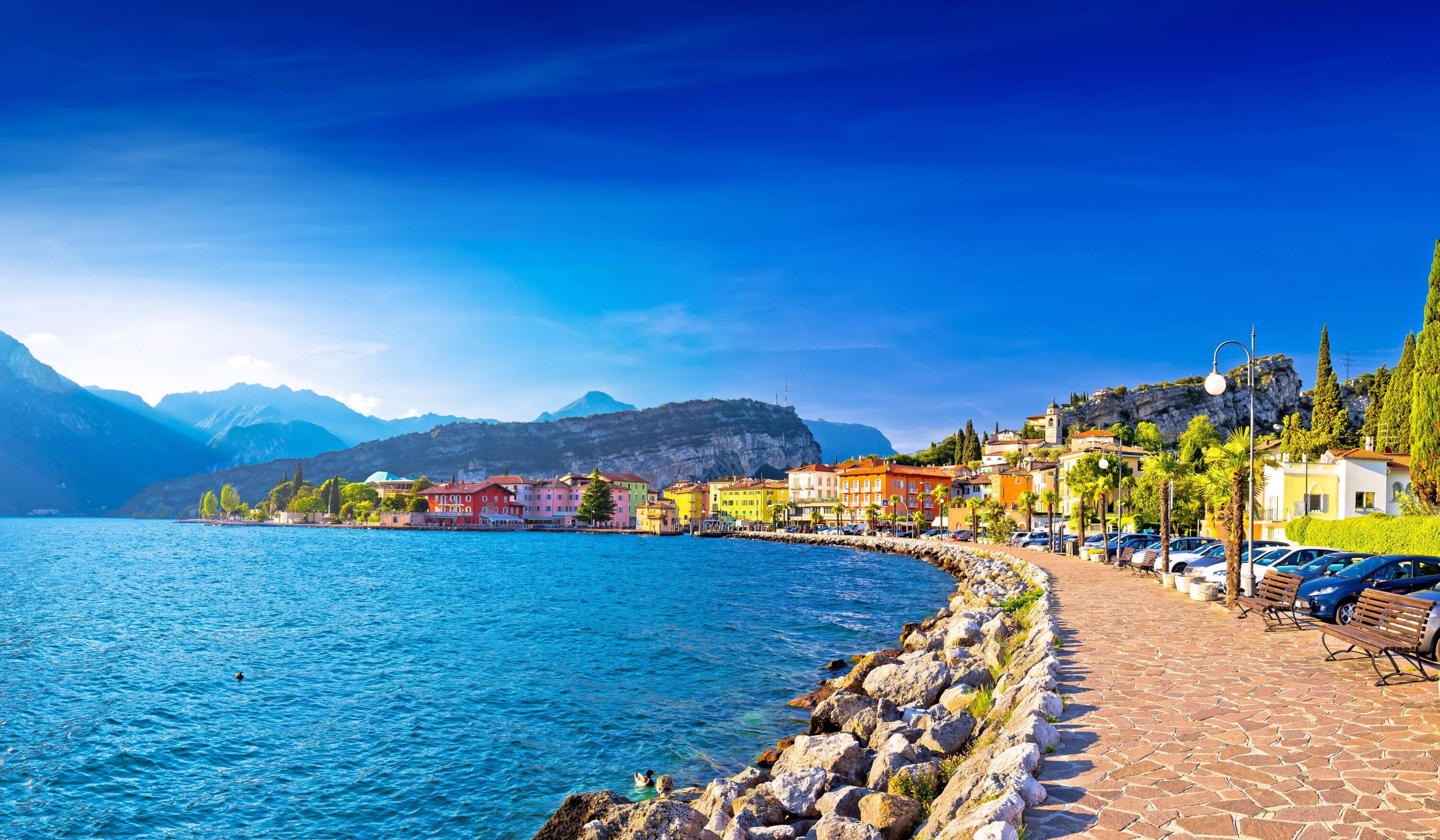 Waterfront in Torbole, Lake Garda, showing pavement and buildings and mountains in the distance