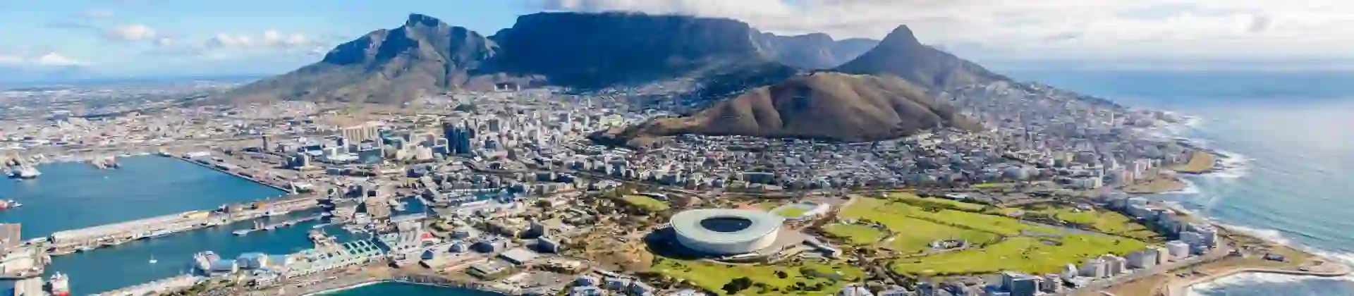 Aerial view of Cape Town, South Africa, showing the city nestled between Table Mountain and the Atlantic Ocean, with the coastline, harbour, and urban landscape clearly visible