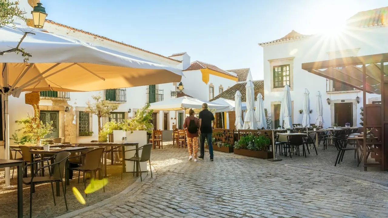 Cobbled streets of Faro on the Algarve with two people walking past traditional white Portuguese buildings and restaurants