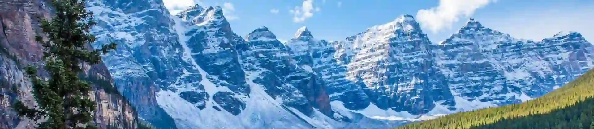 Snow-capped Rocky Mountains towering over the serene, turquoise Moraine Lake in Canada, with dense pine forests lining the shores and a clear blue sky above