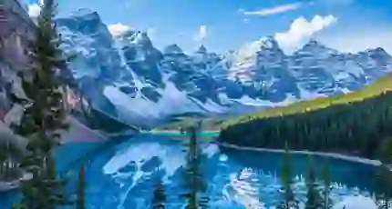 Snow-capped Rocky Mountains towering over the serene, turquoise Moraine Lake in Canada, with dense pine forests lining the shores and a clear blue sky above