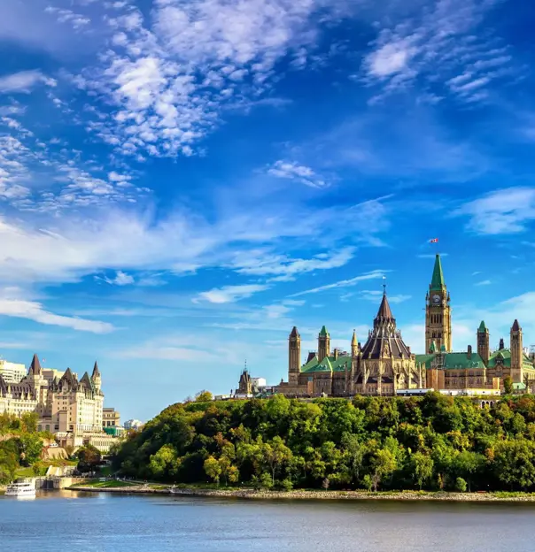 Ottawa skyline in Canada, showing Parliament Hill buildings above a river with trees in the foreground