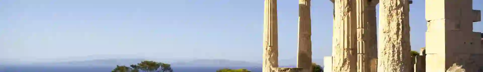 Ancient Greek temple ruins on an island with weathered stone columns overlooking the blue sea and distant mountains under a clear sky
